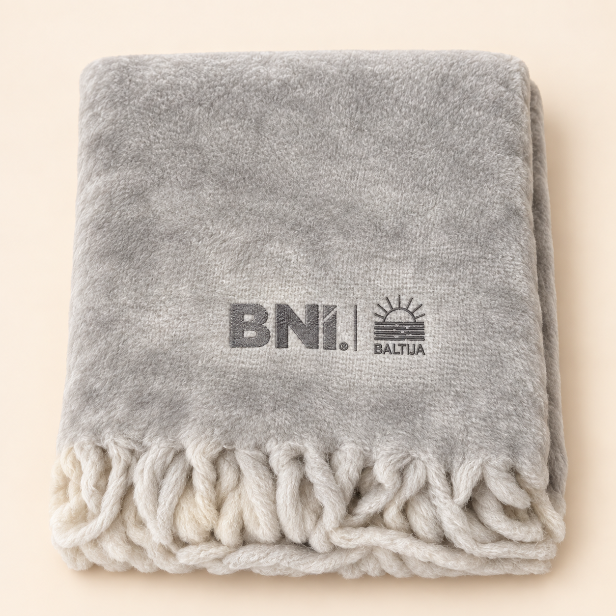 Pilkas pledas su išsiuvinėtu BNI Baltija logotipu kreminiame fone