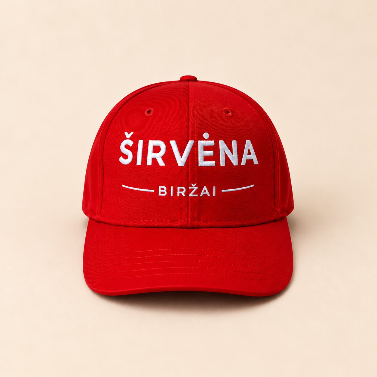 Raudona kepurė su baltai išsiuvinėtu „Širvėna Biržai“ logotipu šiltame kreminiame fone